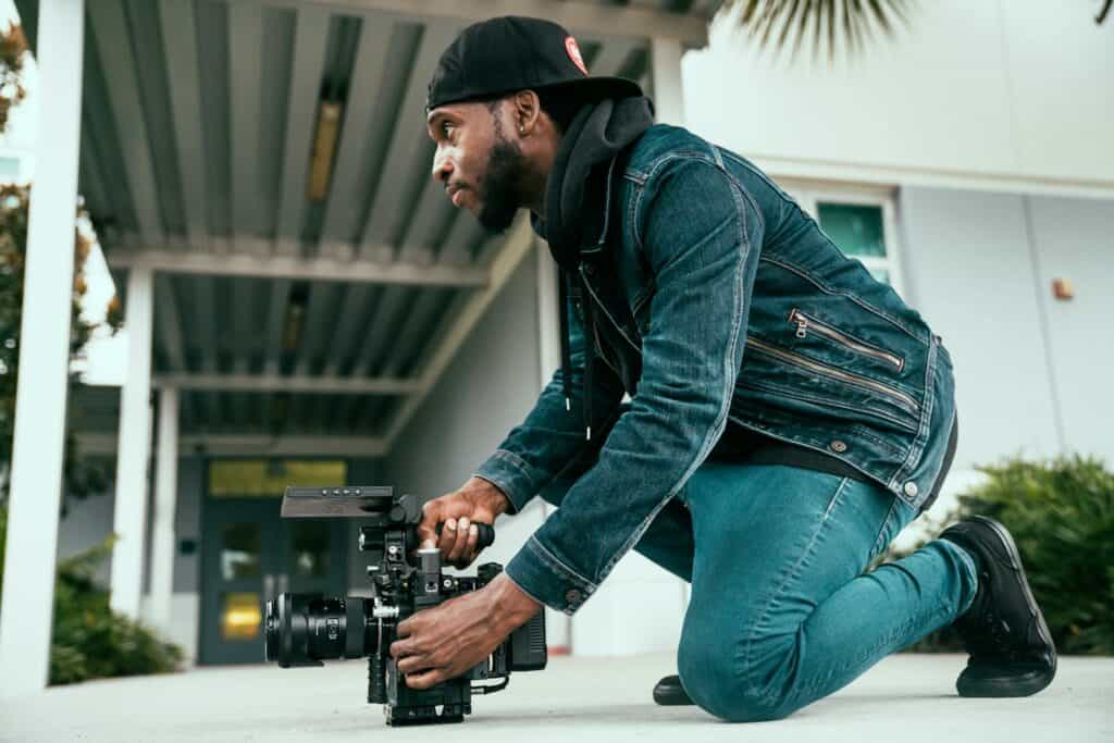 Werbevideo erstellen mit Körpereinsatz: Kameramann kniet mit Kamera am Boden